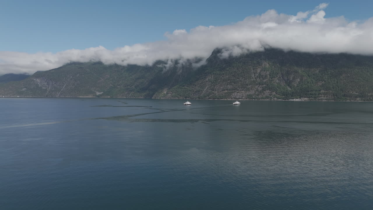 노르웨이의 피오르드를 가로지르는 두 개의 자동차 페리의 드론 은 은 날, 은 물과 반사, 그리고 그들 사이에 구름이 있는 배경의 산.