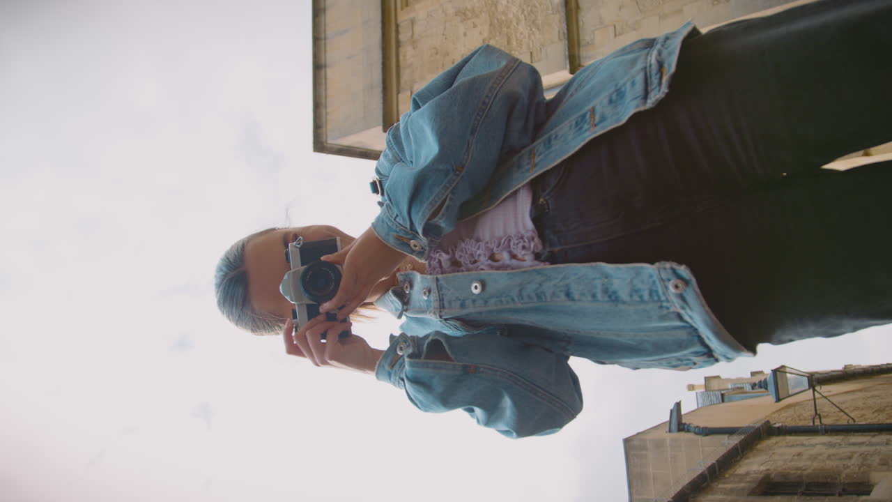 video vertical de una mujer en la calle tomando fotos con una cámara digital de estilo retro para publicar en las redes sociales