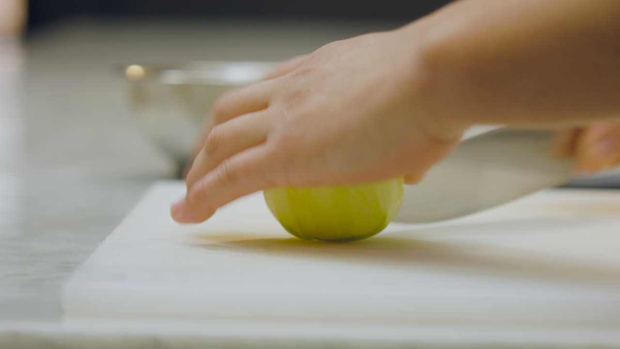 Close-up of a chef's hands cutting a peeled green apple into thin slices on a white chopping board and carefully placing them in an aluminum mold on a kitchen counter
