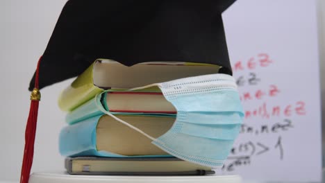 a protective medical mask and a black square hat of a university graduate are attached to the books folded in a column. education concept
