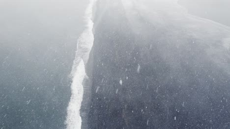 snow storm over hvalnes black sand beach in iceland, high angle drone aerial view