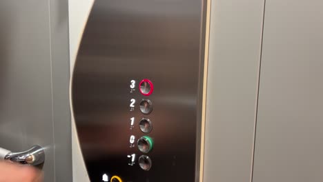 Male-hand-pressing-button-in-a-modern-elevator,-going-up-to-third-level