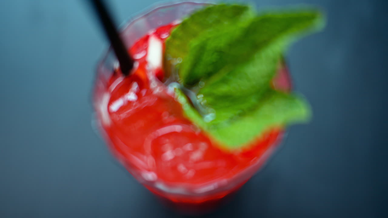 A red drink with ice and mint in a transparent glass, on a blue background