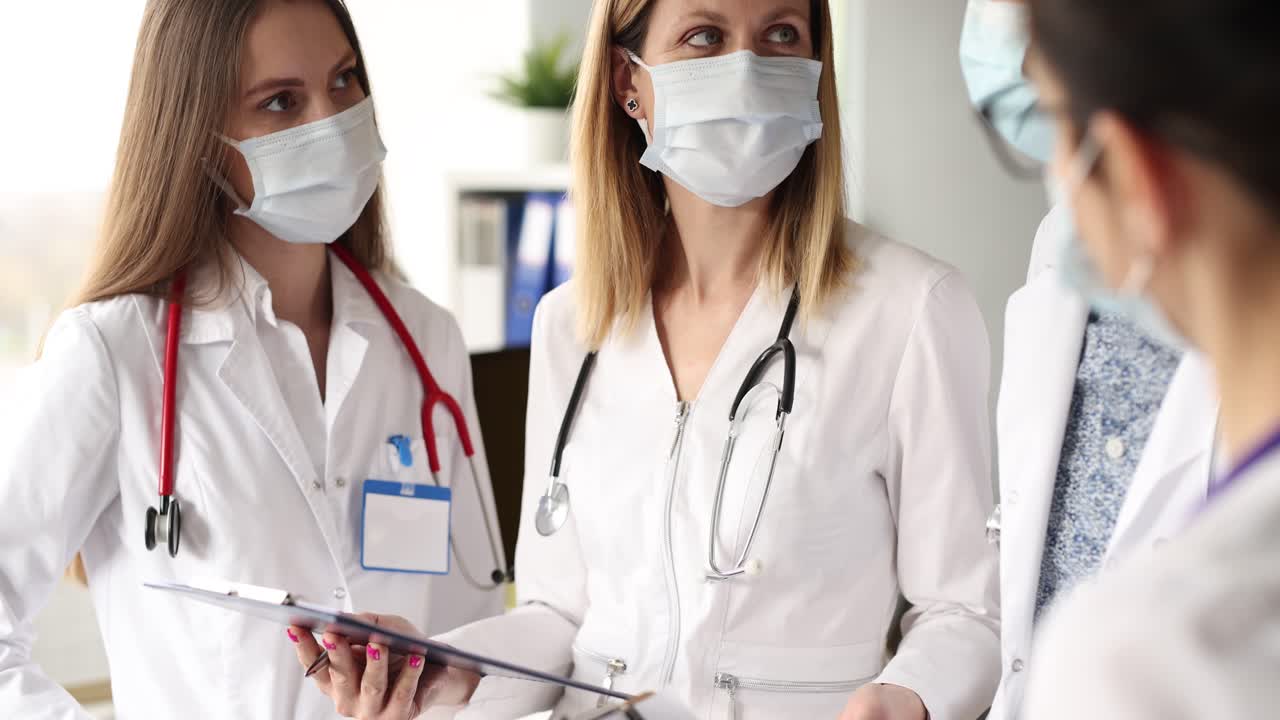 Skupina lékařů v ochranných lékařských rouškách probírá vyšetření pacienta, 4k video.