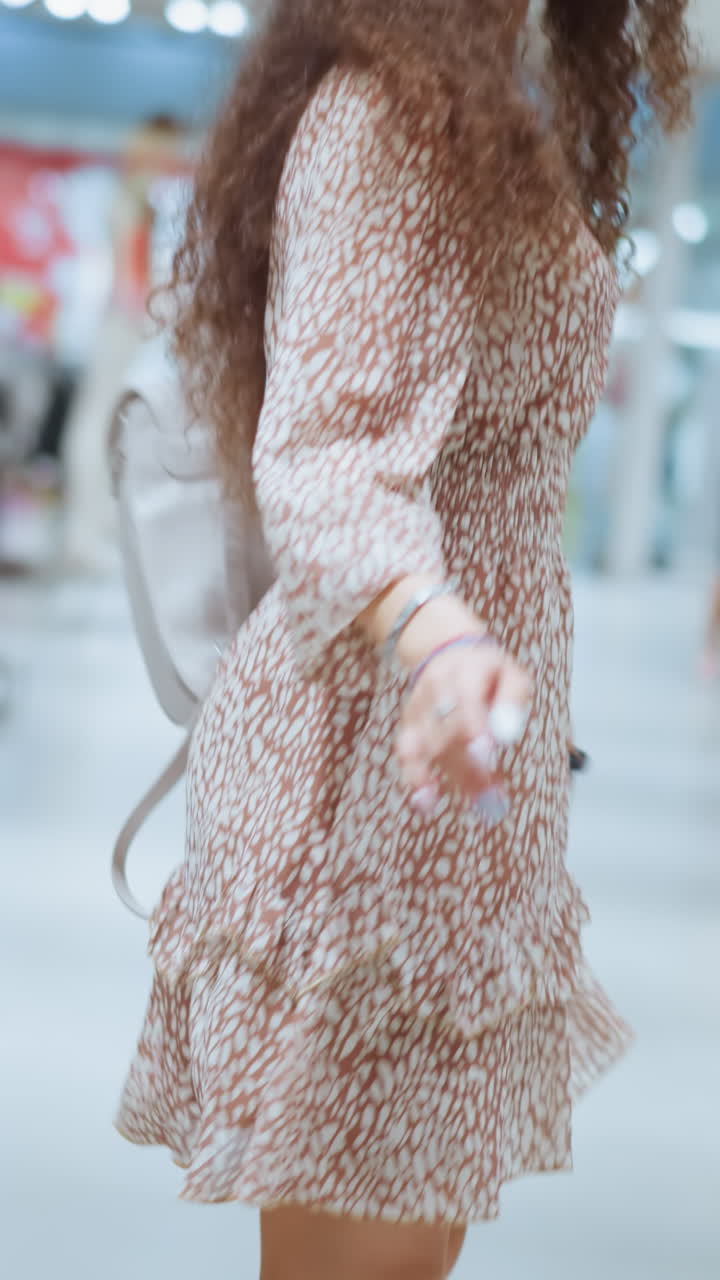 빈티지 드레스를 입은 미소 짓는 여성이 밝은 빛으로 조명된 의류 가게에서 행복하게 춤을 추며 기과 흥분을 표현하고, 다른 쇼핑객들이 배경에 보입니다.