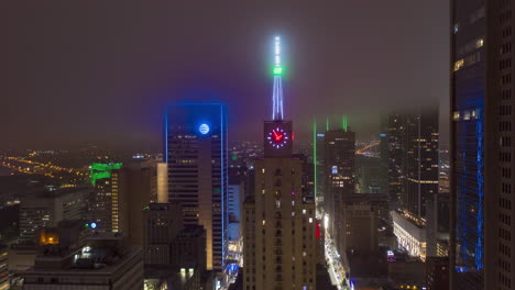 Evening-hyper-lapse-footage-of-high-skyscrapers-in-business-district,-Dallas,-USA.-View-from-drone-flying-towards-big-neon-clock-on-top-of-building