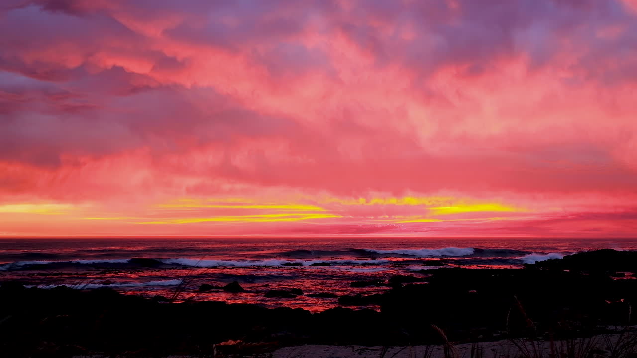 Fire sunset over ocean with rocky coastline, vibrant and warm colors in sky