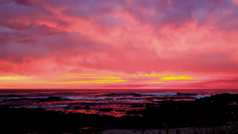 fire sunset over ocean with rocky coastline, vibrant and warm colors in sky