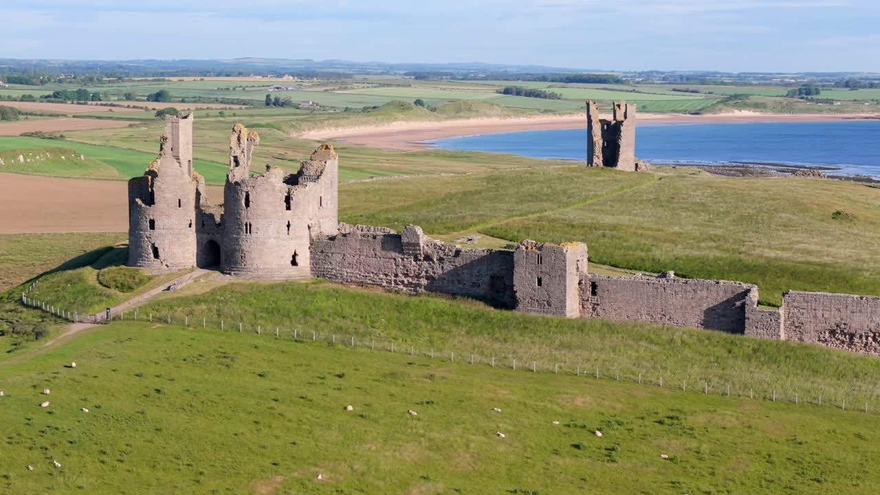 Aerial footage of Dunstanburugh castle ruins on a summer morning with no people