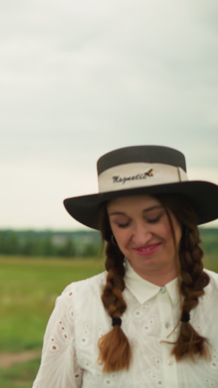 una pareja está de pie en un campo verde con una tabla de arte delante de ellos. el hombre lleva una camisa a cuadros y un sombrero, mientras que la mujer está vestida con un vestido blanco y un sombreiro de borde ancho
