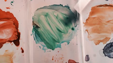 mixing green watercolor paint on a palette, view from above