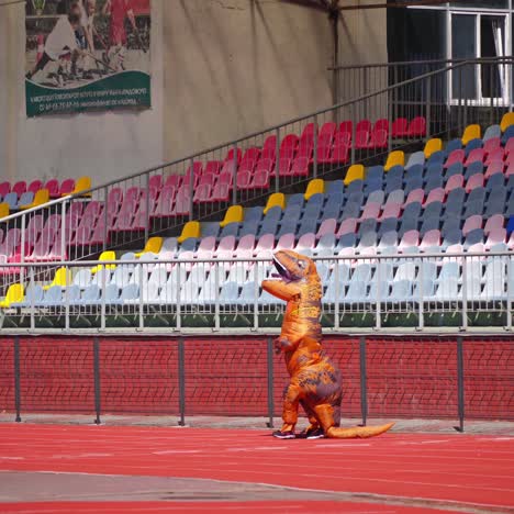 big blow-up dragon suit outdoors. person in a funny dragon costume running happily on the red stadium.