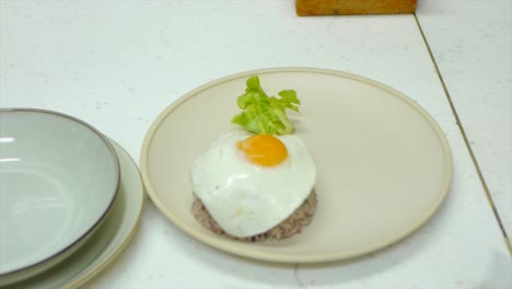 freshly fried egg being placed on top of served rice in kitchen