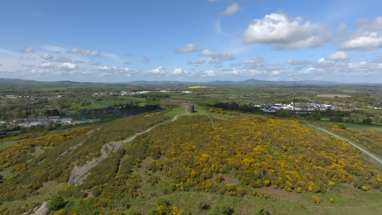Vinegar Hill, Enniscorthy, County Wexford, Ireland, April 2025. Drone stunning panoramic establishing pullback showcases rocky cliff band rising to tower monument and low dense shrub vegetation.