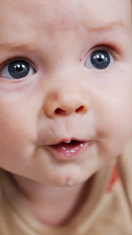 face of a sweet little caucasian infant. close up. lovely grey-eyed baby looking up with surprise. vertical video