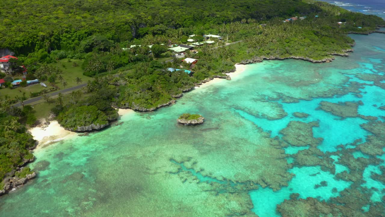 un dron captura una toma que se precipita hacia una costa tropical, mostrando la exuberante vegetación verde, las aguas cristalinas y una pequeña isla rocosa al frente