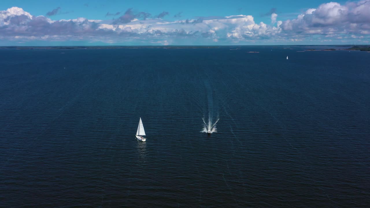 Aerial view of a motorboat passing a white sailboat on the open sea, at the Gulf of Finland, on a sunny, summer day, near Hanko, in Uusimaa, Finland - rising, drone shot