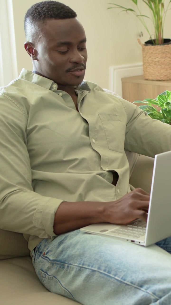 Vertical video: Glancing man in green shirt working on laptop at home, reacting to offscreen motion