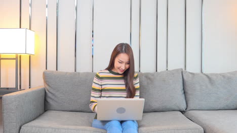 an attractive young woman sitting on a couch inputs data into her laptop