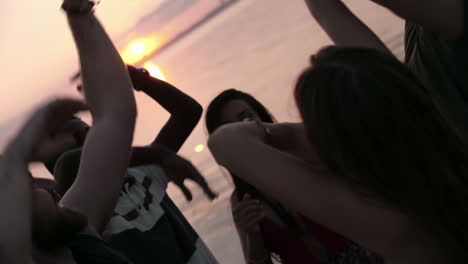 group of friends having fun and dancing raising their arms in a party at sunset