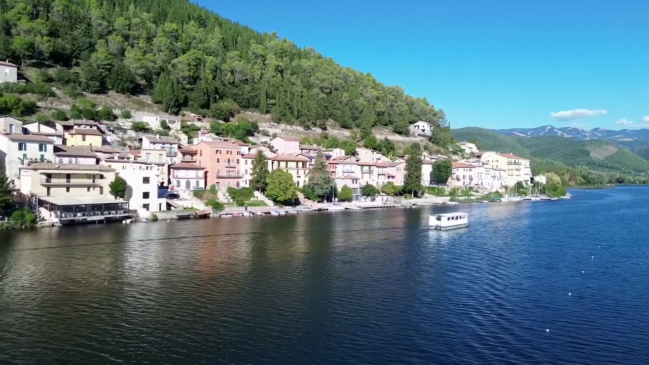 İtalya'nın Umbria bölgesindeki Piediluco köyünün, sakin mavi suları ve yeşil dağların huzurlu bir doğal ortam yarattığı göl kıyısında konumlanmış manzaralı drone çekimi