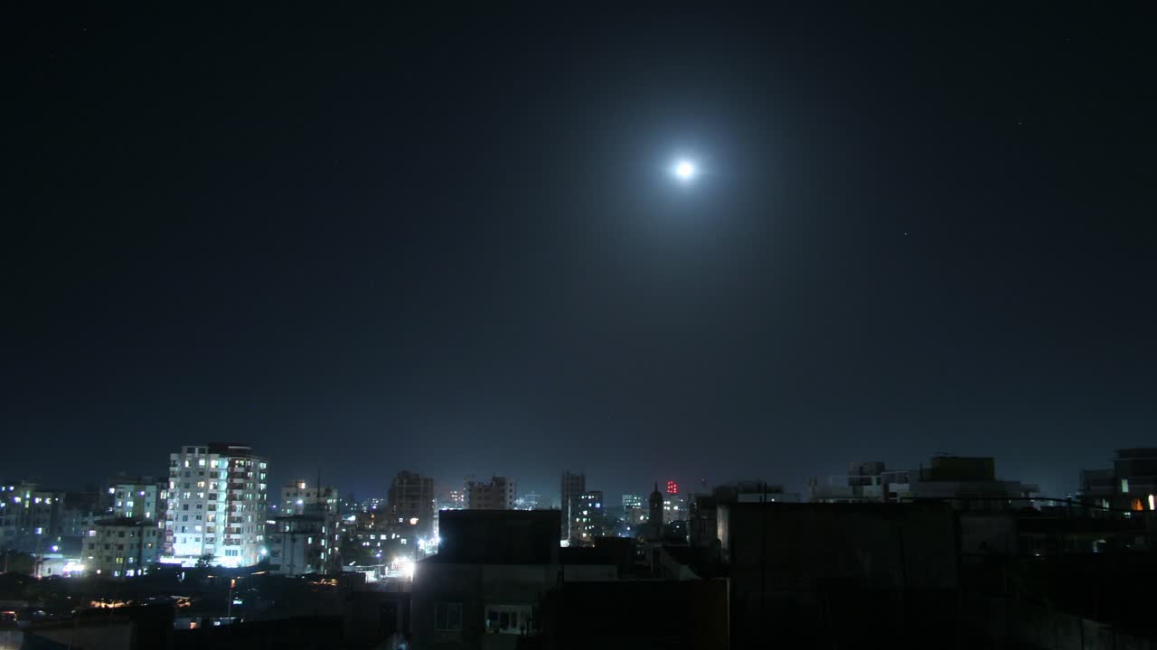 A mesmerizing timelapse of Dhaka's cityscape, with the moon gradually setting over the skyline, capturing the transition from night to dawn.