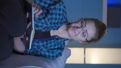Vertical-video-of-Happy-woman-at-home-at-night-keeping-a-diary.-Woman-both-thinks-and-writes.