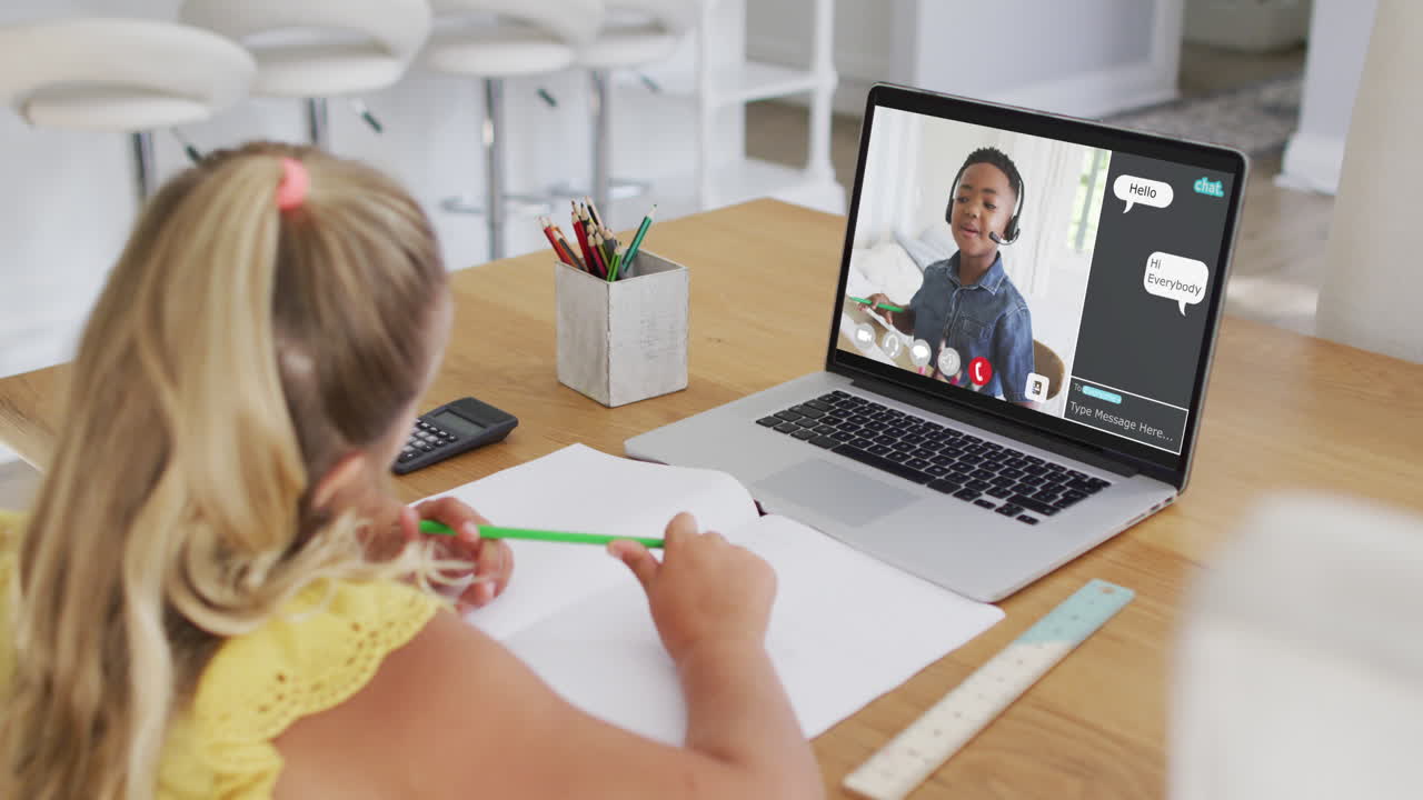 Schoolgirl using laptop for online lesson at home, with school friend and web chat on screen