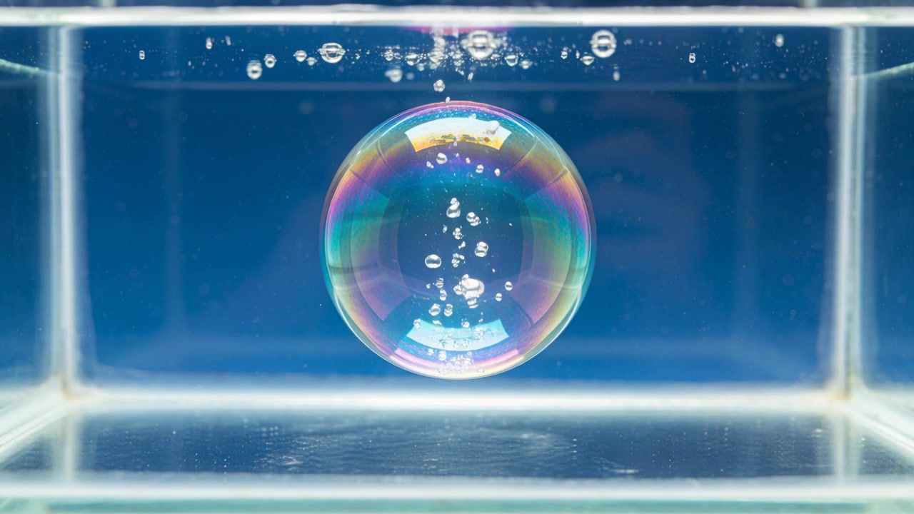 ガラスの水槽の中で、小さな泡が大きな虹色の球体を通り抜け、表面へと上昇していく。