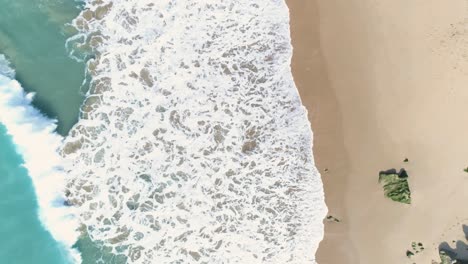 aerial view of powerful turquoise blue sea waves breaking on the sand of a beautiful white sand beach with surfers in the water