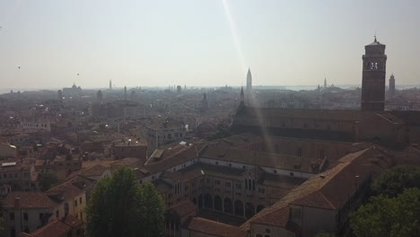 Sunny-lens-flare-low,-hazy-aerial-over-rooftops-of-Venice,-Italy