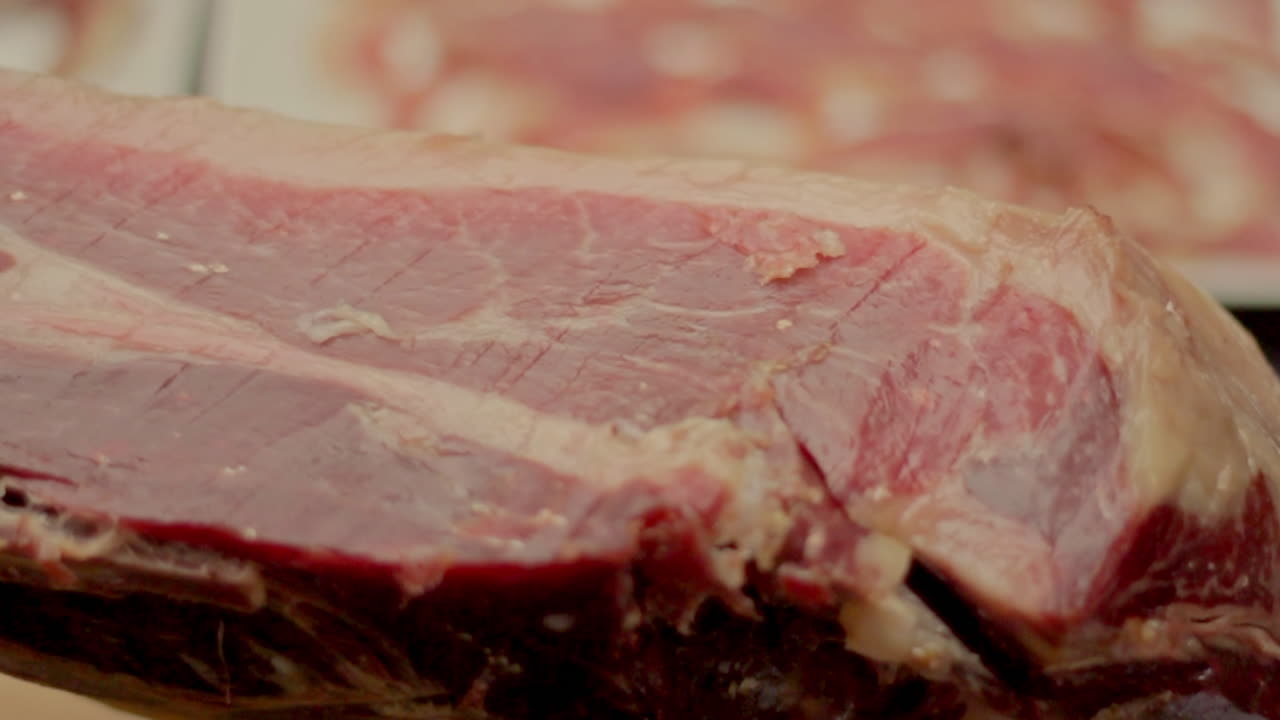 A detailed closeup of a whole leg of cured ham resting on a wooden board ready for slicing