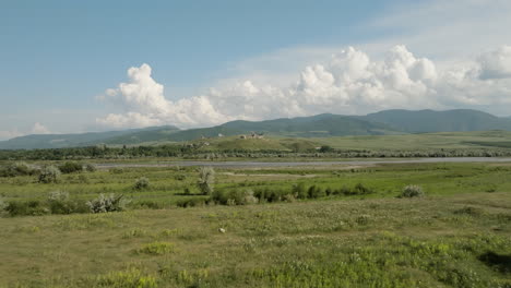 paisaje de pradera junto al río en georgia, castillo samtsevrisi en la distancia