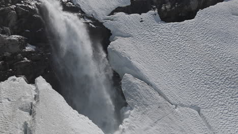 slowmotion drone shot flying around a powerfull waterfall near langvatnet lake in norway close to the strynefjellsveg breaking through ice and snow on a sunny day surrounded by shiny rocks log