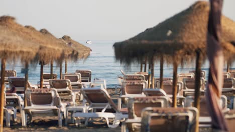 empty sunbeds at the beach with jetski passing by in slow motion