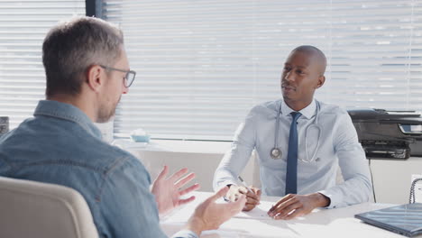 mature male patient sitting at desk having consultation with doctor in office