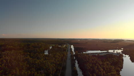 aerial view of a long straight road with a car driving next to a large forest and some ponds in florida