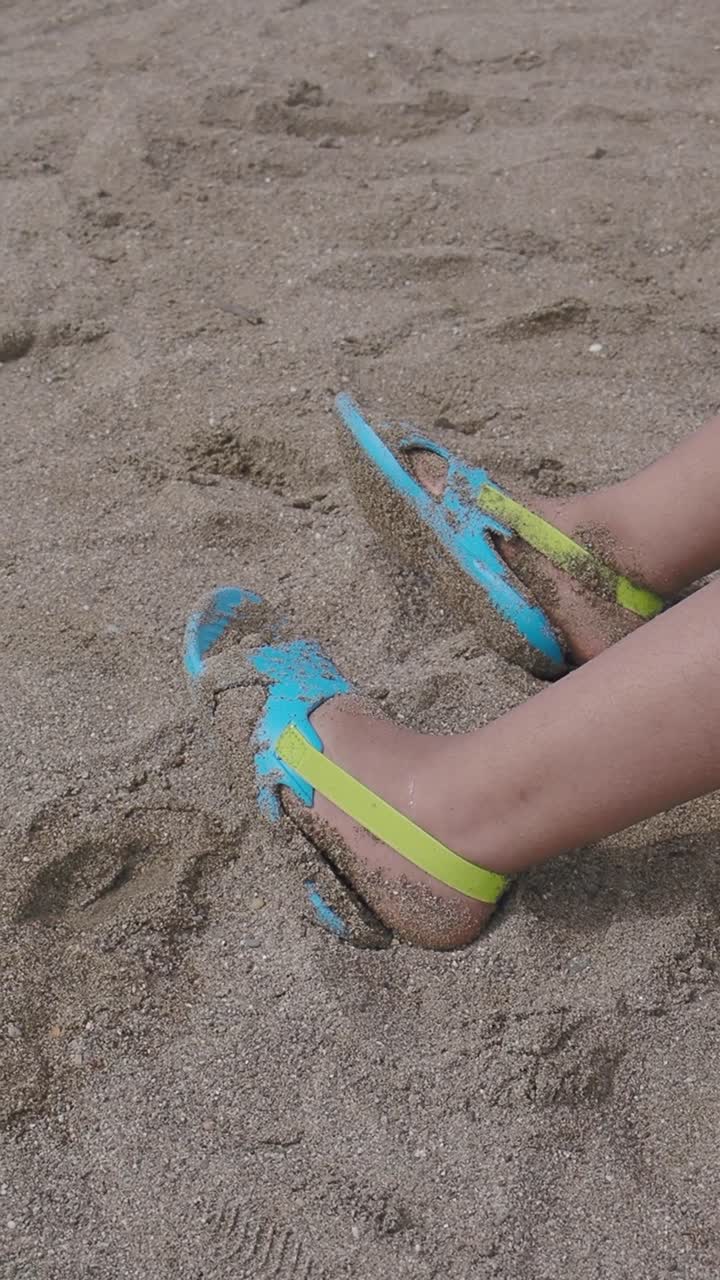 Primo piano di piedi nella sabbia con sandali blu e gialli