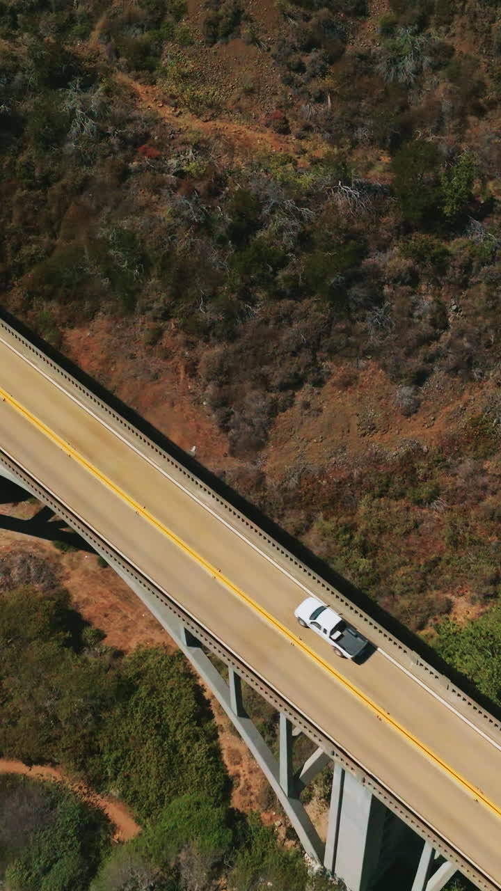 Mountains connected by the arch bridge with cars moving by. Drone descending above the rocks covered with moss. Vertical video