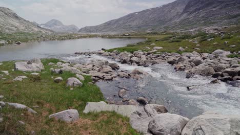 una corriente glacial desciende en un prístino lago alpino en lo alto de las montañas.