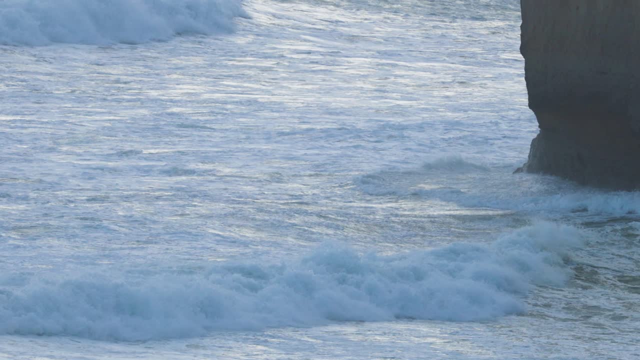 Dynamic ocean waves crash against the iconic limestone stacks of the Twelve Apostles, captured in natural lighting along the Great Ocean Road