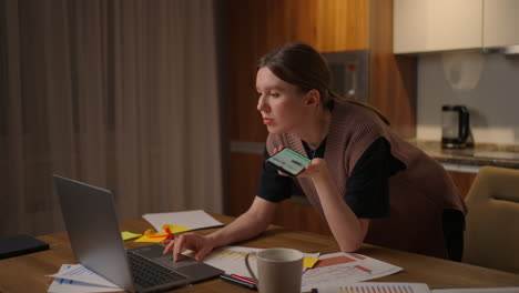 woman paying bill payment online with mobile phone at home. caucasian woman in beige sweater and using smartphone or cell phone. tapping scrolling watching video content bloggs.