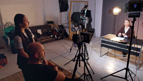 male and female backstage staff looks at the blogger sitting at desk. modern equipment is taking video of the brunette lady. blog content creation.