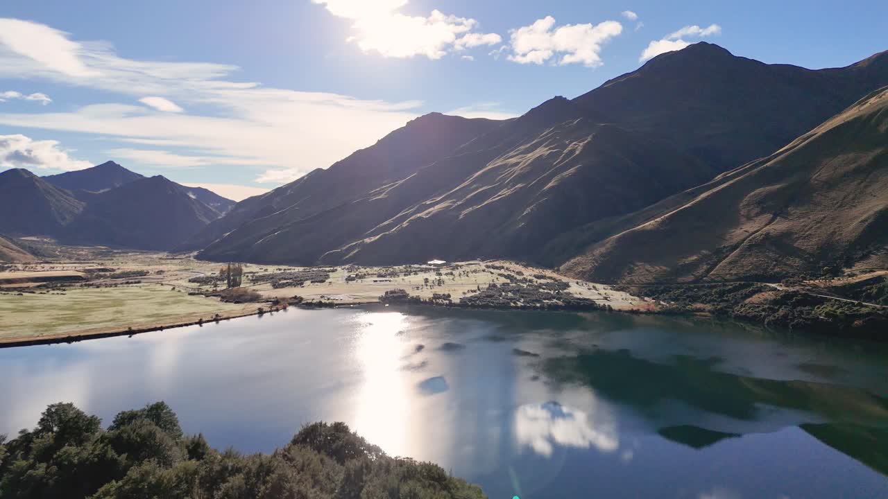 Aerial footage captures Lake Moke's serene beauty in Queenstown, New Zealand, with stunning mountain reflections and dynamic lighting
