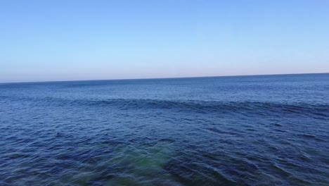 Drone-Shot-of-Pacific-Ocean-in-Malibu,-California-with-Waves-crashing-at-Sunset-on-a-Sunny-Day