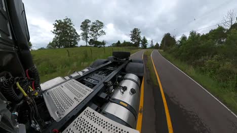 rear view perspective of truck driving a on a country road under a cloudy sky with woods on both sides