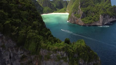 a drone reveal shot of maya bay with rocky cliffs while a boat cruising