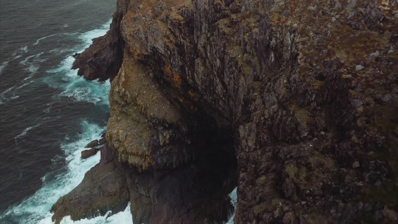 Rugged coastal cliffs and blue water turns white with foam as waves crash into them