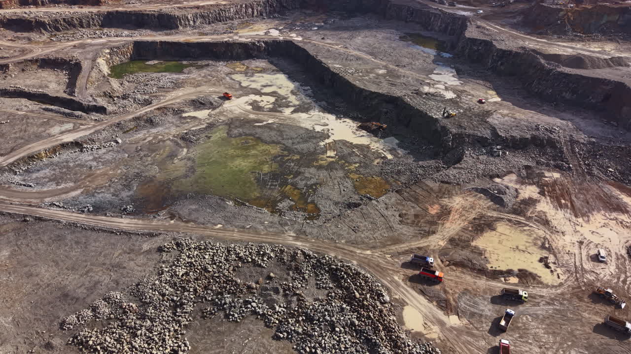 Workers extract granite from a large quarry while machinery operates at different areas during daytime in a busy stone mining location