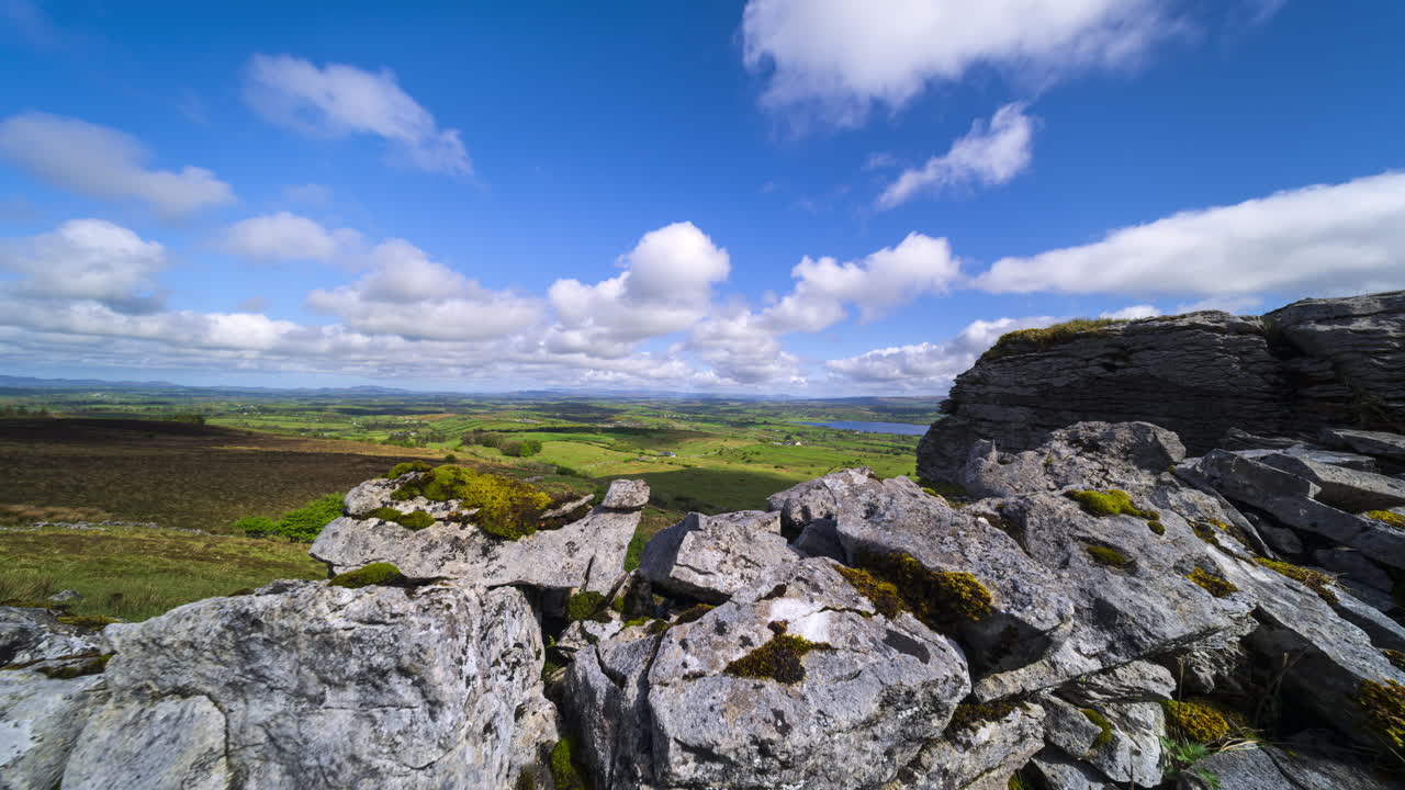 İrlanda, Sligo bölgesindeki Carrowkeel'den güneşli ve bulutlu bir günde, ön planda taş duvar, uzakta tepeler ve göl manzarasıyla kırsal alanın panoramik hareketli hızlandırılmış çekimi
